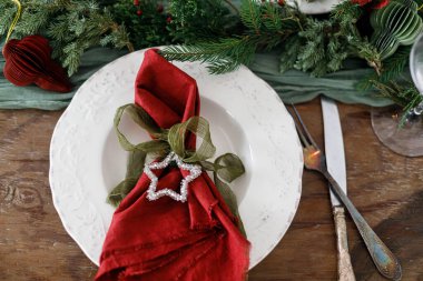 Aile yemeği için şık bir Noel sofrası. Peçeteli, yıldızlı, çatal bıçaklı, cam, kurdeleli, yeşil köknar dallı, ahşap masada duran zarif bir tabak. Noel Tatil Zamanı