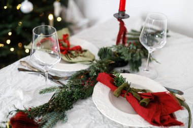 Aile yemeği için şık bir Noel sofrası. İçinde peçeteler, çatal bıçak takımı, cam kaşık, kurdele, yeşil köknar dalları, kırmızı böğürtlen ve keten masa örtüsü üzerine mum olan zarif bir tabak. Tatil zamanı.