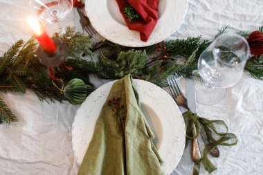 Aile yemeği için şık bir Noel sofrası. İçinde peçeteler, çatal bıçak takımı, cam, kurdele, yeşil köknar dalları, masa örtüsünün üzerinde kırmızı böğürtlen ve mum bulunan zarif bir tabak. Tatil zamanı.