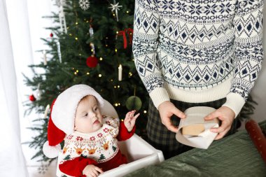 Mutlu bir baba ve Noel Baba şapkalı şirin bir oğlan Noel hediyelerini şık dekore edilmiş ağacın arka planında paketliyor. Mutlu Noeller ve mutlu tatiller! Atmosferik aile zamanı.