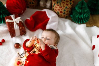 Şenlikli süveter giyen, altın ışıklarla örtülü, Noel ağacının altında hediyeli, güzel bir erkek bebek. Mutlu Noeller! Atmosferik tatil zamanı, aile süsleme ağacı.