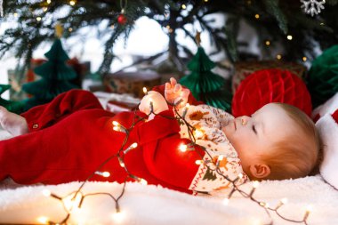 Noel ağacının altında, üzerinde altın ışıklar olan, Noel süveteri içinde şirin bir erkek bebek. Mutlu Noeller! Atmosferik tatil zamanı, aile süsleme ağacı.