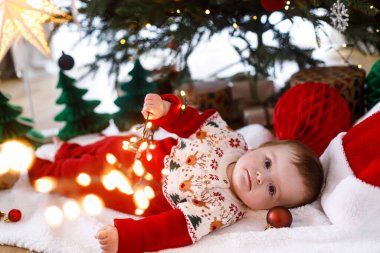 Şenlikli süveter içinde Noel ağacının altında battaniyeye uzanmış altın ışıklarla oynayan tatlı bir bebek. Mutlu Noeller! Atmosferik tatil zamanı, aile süsleme ağacı.