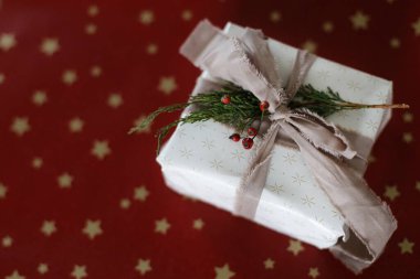 Kırmızı kağıdın üzerinde duran şık bir Noel hediyesi. Mutlu Noeller ve mutlu tatiller! Keten kurdeleli Xmas hediyesi ve sedir dalı, kopyalama alanı. Bayram bayrağı