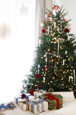 Mutlu Noeller ve mutlu tatiller! Paketlenmiş şık Noel hediyeleri ipek yaylar, yeşil dal ve böğürtlenler, kırsal masadaki süslere karşı dekore edilmiş yılbaşı ağaçları..