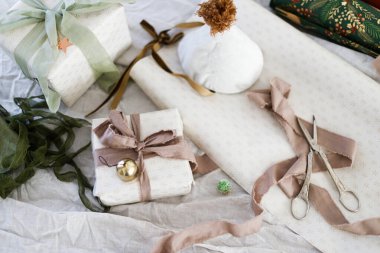 Mutlu Noeller ve mutlu tatiller! Çarşaf kurdelesi, çan, makas ve kırsal masa yatağında duran şenlikli ambalaj kağıdıyla şık bir Noel hediyesi. Bayram hediyelerini paketliyorum.