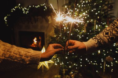 Mutlu yıllar! Geceleri yılbaşı ağacı altın ışıklarının arka planında yanan maytaplar. Çifte ellerde parlayan havai fişekler, yeni yıl arifesi kutlaması