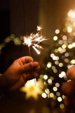 Noel ağacı ışıklarına karşı havai fişek tutan eller akşam sıcacık oturma odasında sallanıyor. Yeni yılınız kutlu olsun! Atmosferik aile kutlaması, ellerinde yanan maytaplarla.