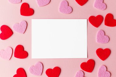 Sevgililer Günü kartı modeli. Boş tebrik kartı düz pembe ve kırmızı kalplerle pembe kağıt üzerinde yatıyordu. Sevgililer Günü kartpostalınız kutlu olsun.