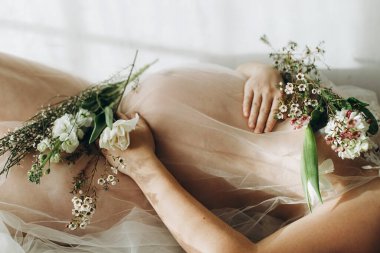 Güzel hamile bir kadın elinde çiçeklerle bebek şişliği tutuyor ve uzanıyor. Anneler Günün kutlu olsun! Sağlıklı hamilelik ve doğurganlık kavramı. Peçeli hamile kadın, hassas annelik.