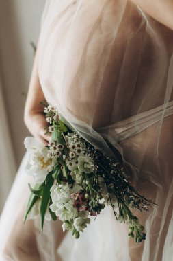 Güzel hamile bir kadın kucağında bebek şişliği, çiçekler ve yumuşak ışıkta poz veriyor. Anneler Günün kutlu olsun! Sağlıklı hamilelik ve doğurganlık kavramı. Peçeli hamile kadın, hassas annelik.