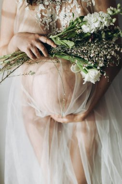 Güzel hamile bir kadın kucağında bebek şişliği, çiçekler ve yumuşak ışıkta poz veriyor. Anneler Günün kutlu olsun! Sağlıklı hamilelik ve doğurganlık kavramı. Peçeli hamile kadın, hassas annelik.