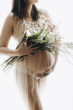 Güzel hamile bir kadın kucağında bebek şişliği, çiçekler ve yumuşak ışıkta poz veriyor. Anneler Günün kutlu olsun! Sağlıklı hamilelik ve doğurganlık kavramı. Peçeli hamile kadın, hassas annelik.