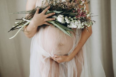 Güzel hamile kadın elinde çiçeklerle bebek şişliği tutuyor. Yaklaş. Anneler Günün kutlu olsun! Sağlıklı hamilelik ve doğurganlık kavramı. Peçeli hamile kadın, hassas annelik.