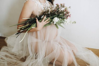 Güzel hamile kadın elinde çiçeklerle bebek şişliği tutuyor. Yaklaş. Anneler Günün kutlu olsun! Sağlıklı hamilelik ve doğurganlık kavramı. Peçeli hamile kadın, hassas annelik.