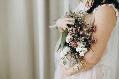 Elinde bebek şişliği ve güzel çiçekler olan şık hamile bir kadın. Sağlıklı hamilelik ve doğurganlık kavramı. Anneler Günün kutlu olsun! Peçeli hamile kadın poz veriyor ve nazikçe karnına sarılıyor.