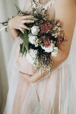 Güzel hamile kadın elinde çiçeklerle bebek şişliği tutuyor. Yaklaş. Anneler Günün kutlu olsun! Sağlıklı hamilelik ve doğurganlık kavramı. Peçeli hamile kadın, hassas annelik.