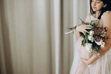 Güzel hamile bir kadın elinde çiçeklerle poz veriyor. Anneler Günün kutlu olsun! Sağlıklı hamilelik ve doğurganlık kavramı. Peçeli hamile kadın, hassas annelik.