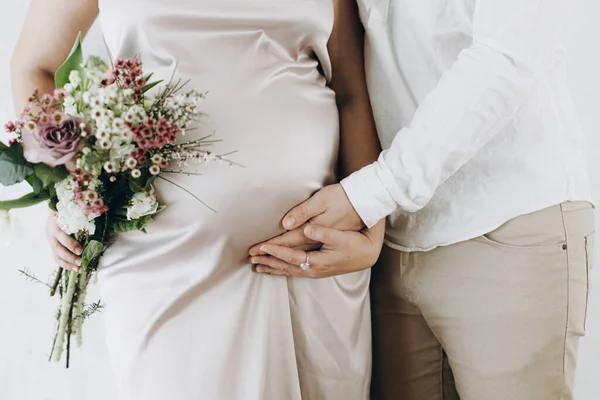 Koca, güzel çiçeklerle şık hamile kadınlara sarılıyor. Sağlıklı hamilelik ve doğurganlık kavramı. Anneler Günün kutlu olsun! İpek elbiseli hamile kadın.