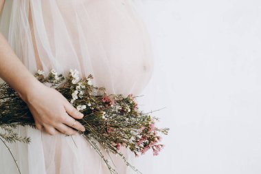 Güzel hamile bir kadın kucağında bebek şişliği, çiçekler ve yumuşak ışıkta poz veriyor. Anneler Günün kutlu olsun! Sağlıklı hamilelik ve doğurganlık kavramı. Peçeli hamile kadın, hassas annelik.