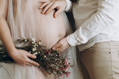 Güzel bir çift hamile bebeğe çiçeklerle sarılıyor. Anneler Günün kutlu olsun! Sağlıklı hamilelik ve doğurganlık kavramı. Koca, ipek elbiseli hamile kadına sarılıyor.,