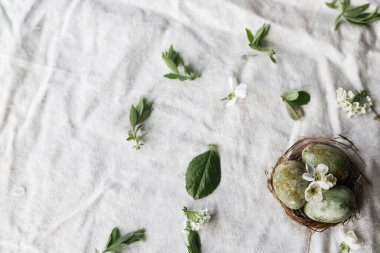 Mutlu Paskalyalar! Yuvadaki doğal boyanmış yumurtalar ve keten arka plandaki bahar çiçekleri düz. Metin, Paskalya tebrik kartı veya asgari afiş için alanı olan bir tatil şablonu
