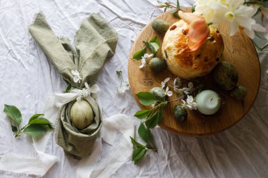 Paskalya kutlaması. Tavşan kulaklı paskalya yumurtaları peçete, paskalya ekmeği, mum ve kiraz çiçekleri çarşafların üzerinde, üst manzara. Atmosferik otantik Paskalya sofrası, durgun yaşam