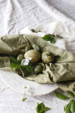 Mutlu Paskalyalar! Tabaktaki yeşil keten peçeteye doğal boyanmış yumurta ve bahar çiçekleri. Paskalya kutlaması masası, tatil durgun hayatı. Tebrik kartı ya da afiş, metin için boşluk