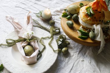 Mutlu Paskalyalar! Tavşan kulaklı şık yumurtalar tabakta peçete, tezgahta paskalya pastası, bahar çiçekleri ve mum. Paskalya kutlaması masası, tatil durgun hayatı. Mevsimler selamlama ya da bayrak