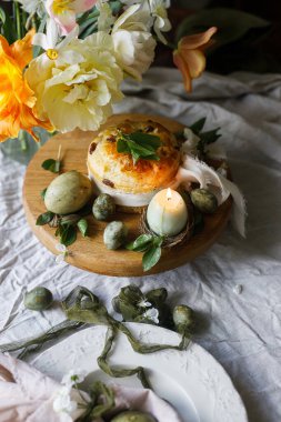 Mutlu Paskalyalar! Tavşan kulaklı şık yumurtalar tabakta peçete, tezgahta paskalya pastası, bahar çiçekleri ve mum. Paskalya kutlaması masası, tatil durgun hayatı. Mevsimler selamlama ya da bayrak