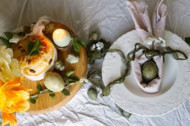 Mutlu Paskalyalar! Tavşan kulaklı şık yumurtalar tabakta peçete, tezgahta paskalya pastası, bahar çiçekleri ve mum. Paskalya kutlaması masası, tatil manzarası. Mevsimler selamlama ya da bayrak