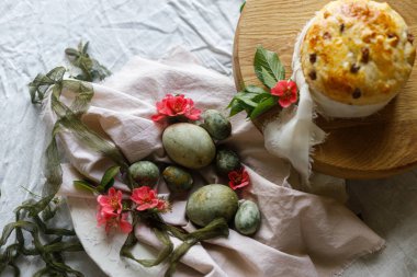 Paskalya kutlaması. Şık yeşil paskalya yumurtaları, paskalya ekmeği ve çarşaf peçetesinde kiraz çiçekleri, yazı için yer. Atmosferik otantik Paskalya tablosu ayarı, üst görünüm