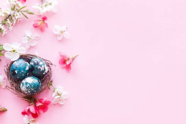 Paskalya düzlüğü. Yuvada zarif paskalya yumurtaları ve pembe arka planda kiraz çiçekleri. Paskalya kutlaması, sezon kutlaması. İlkbahar modern çiçek bayrağı