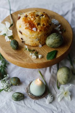 Paskalya kutlaması. Şık yeşil paskalya yumurtaları, paskalya ekmeği, mum ve kiraz çiçekleri keten peçetede, yazı için yer. Atmosferik otantik Paskalya sofrası, durgun yaşam