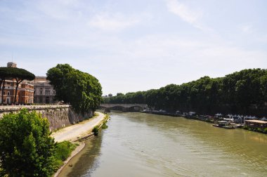 Nehir manzarası ve kemerli köprü. Binalar ve teknelerle dolu nehir dolgusu.