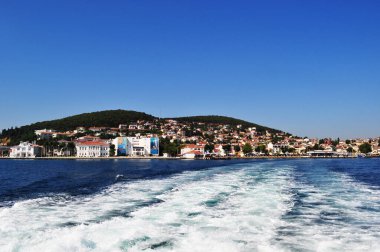 Deniz kıyısının ve evlerin panoramik manzarası. Tekne pervanelerinden köpükle sakin deniz.