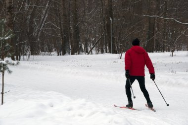 Kış. Kırmızı ceketli bir adam parkta kayak yapıyor..