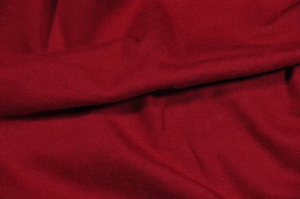 Background, texture. Fragment of red fabric with a small pattern and a fold.