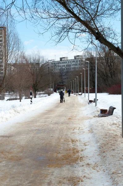 People walk in the park on a sunny winter day. City park and residential buildings background.