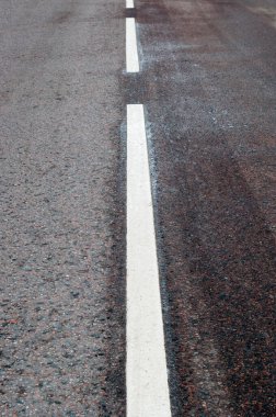 Yakın plan beyaz çizgilerle işaretlenmiş asfalt bir yol..