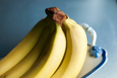 Beyaz bir tabakta birkaç sarı muz. Bulanık mavi arkaplan.