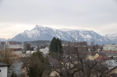 Şehir evlerinin çatılarının panoramik manzarası ve karla kaplı zirveleri..