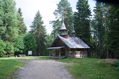 Ağaçlarla kaplı bir ormanın panoramik manzarası ve kütüklerden yapılmış eski bir ahşap kilise. 03 Ağustos 2017, Malye Korely, Arkhangelsk, Rusya.