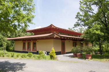 Yeşil ağaçların arka planına karşı kırmızı tek katlı bir evin panoramik görüntüsü.