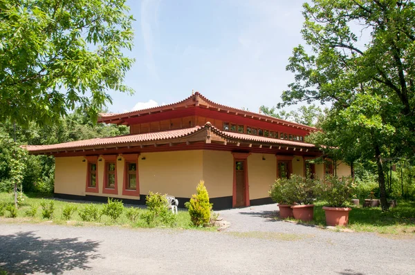 Yeşil ağaçların arka planına karşı kırmızı tek katlı bir evin panoramik görüntüsü.