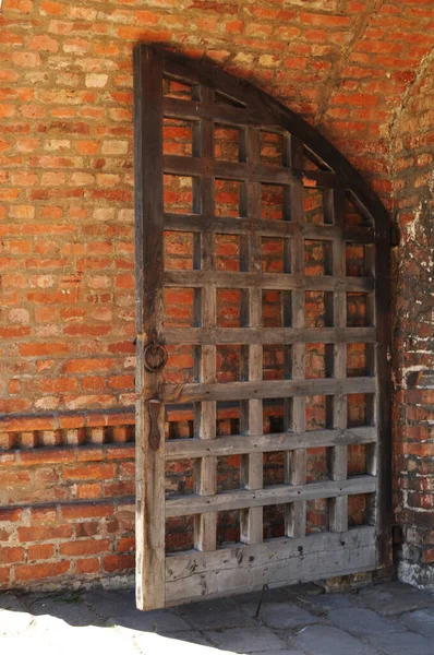 Fragment of the wooden monastery gates. Arch from red old bricks and wooden gates.
