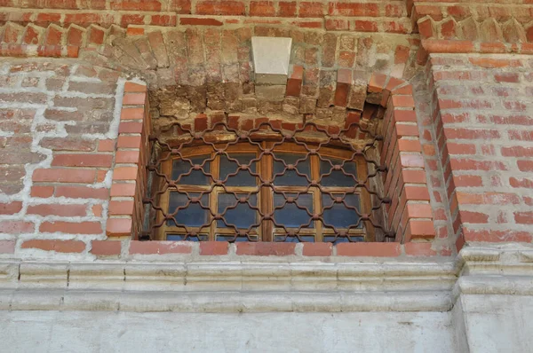 Metal şekilli bir kafesin arkasındaki dikdörtgen pencereye yakın çekim. Manastırın penceresi olan eski tuğla duvarı.