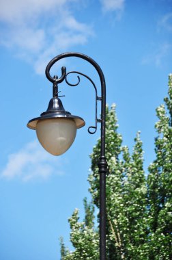 Fener, şehrin ışıkları. Mavi gökyüzü ve yeşil ağaçlardan oluşan bir arka planda fener.