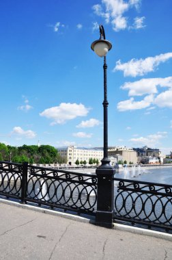 Işık direğinin panoramik görüntüsü, köprü korkuluğu ve baypas yolu. Şehirde güneşli bir gün.