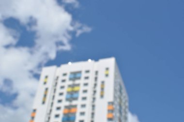Arka plan bulanık. Yeni bir konut binasının odaklı olmayan görüntüsü. Bulutlu mavi gökyüzü.
